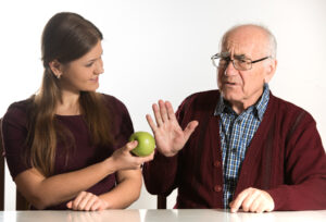 Home care provider assisting senior man in eating a green apple.